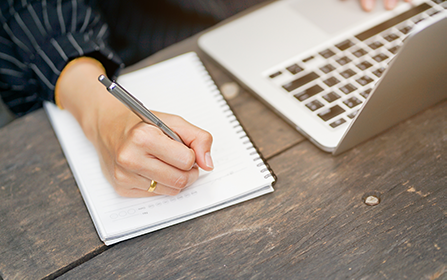 businesswoman hand writing content on notebook and using laptop