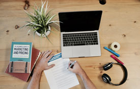 hand writing on paper next to laptop on table