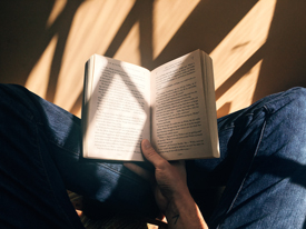 Person reading book next to shadowy window